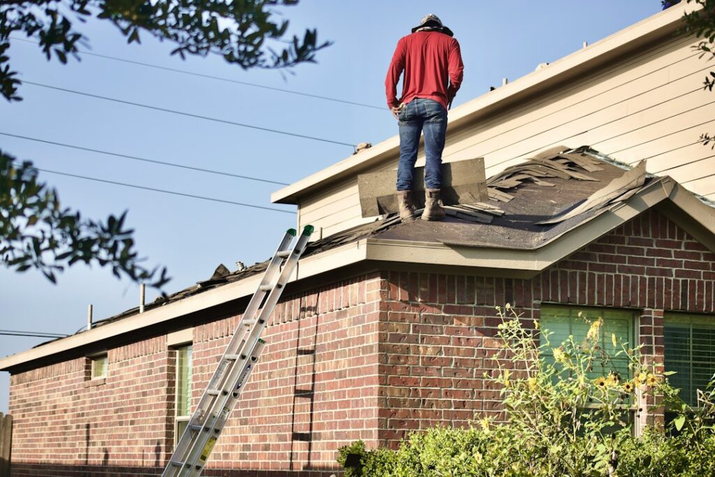 Homeowner reviews roof damage photos and insurance paperwork at a table beside a rain-streaked window.